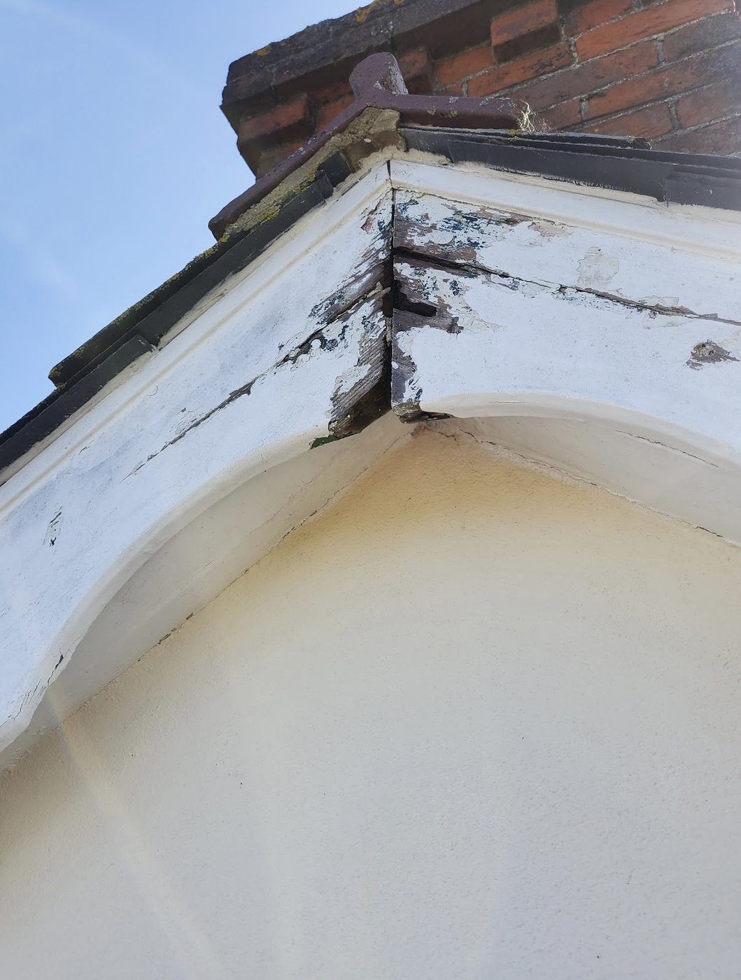 Close-up of a bargeboard with paint flaking away and bare timber showing at the joint