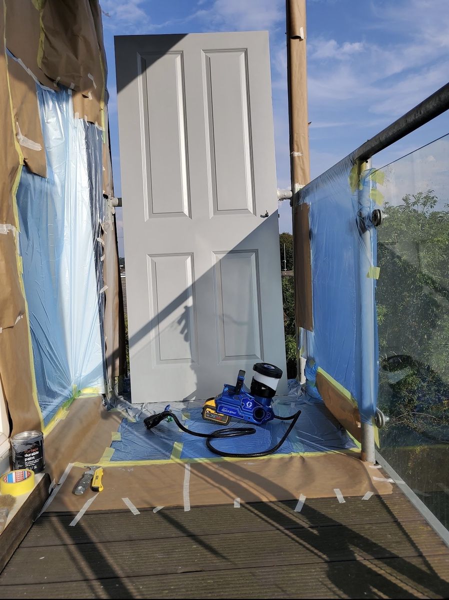 A door set up outside in a masked-off spray booth with the sprayer alongside