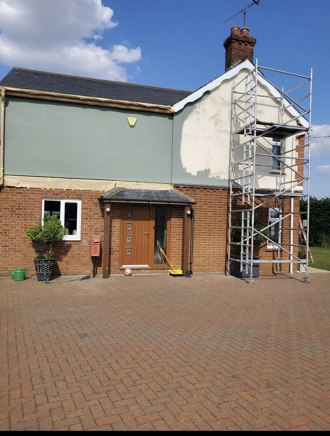A rendered house part-way through repainting, the original cream render still showing on the gable